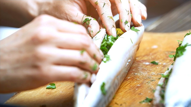 Hands stuffing a raw fish with fresh herbs