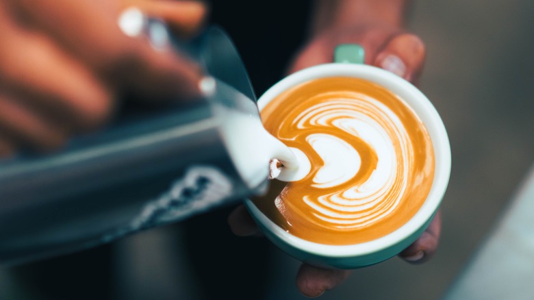 Person pouring steamed milk into a latte