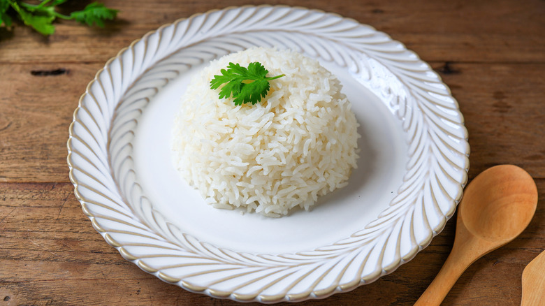 A scoop of jasmine rice and a sprig of parsley on a decorative white plate next to a wooden spoon