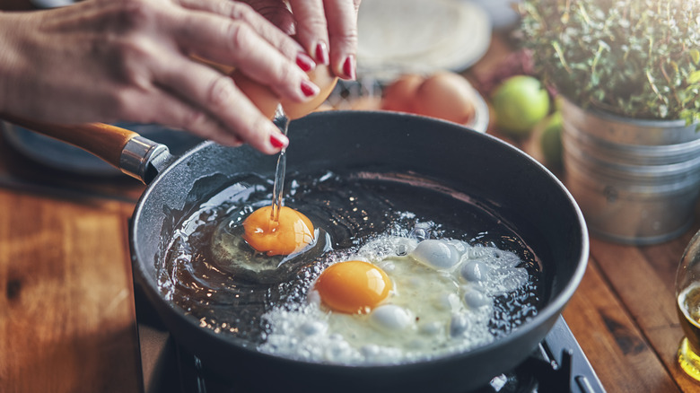 Person cracking eggs into hot pan