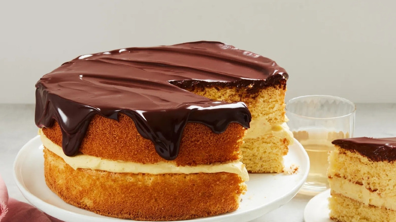 Boston cream pie cake on cake stand with slice cut on white plate