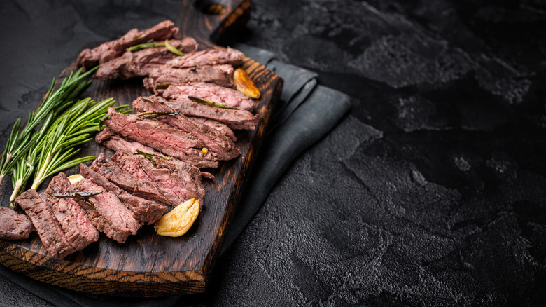 Sliced grilled skirt steak on a wooden cutting board with rosemary and garlic