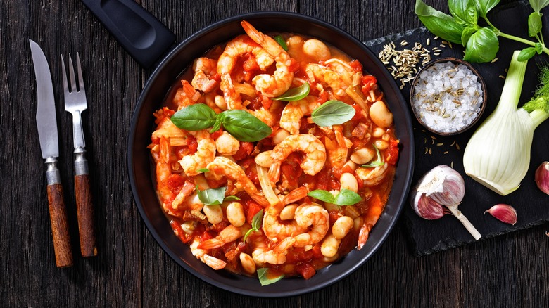 Bean dish with shrimp, tomato sauce, and basil in a black skillet