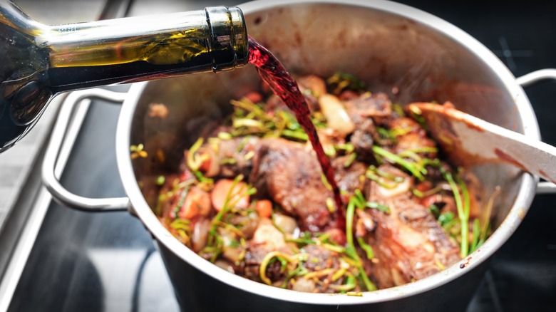 Red wine getting poured into a pot full of meat and other ingredients