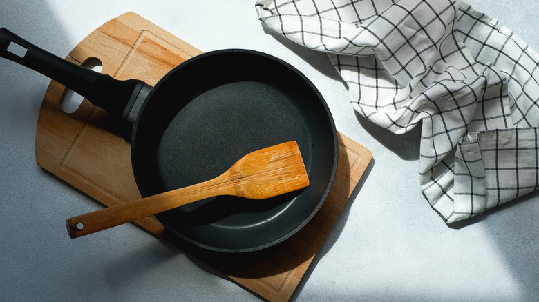 cast iron pan with wooden spatula, cutting board, and kitchen rag