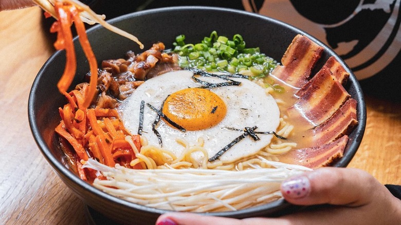 Bowl of ramen soup with realistic vegan egg, vegan brisket, and Asian vegetables