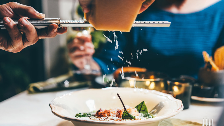 Server grating cheese onto restaurant pasta dish