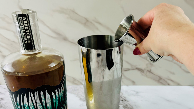 hand pouring jigger over shaker