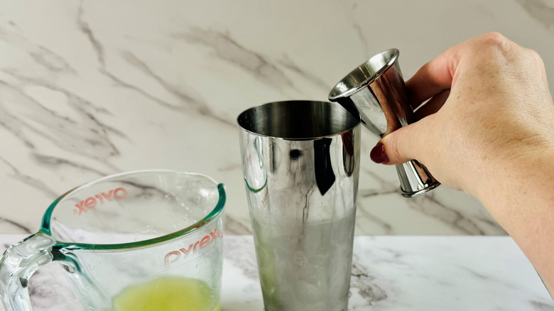 hand pouring jigger over shaker