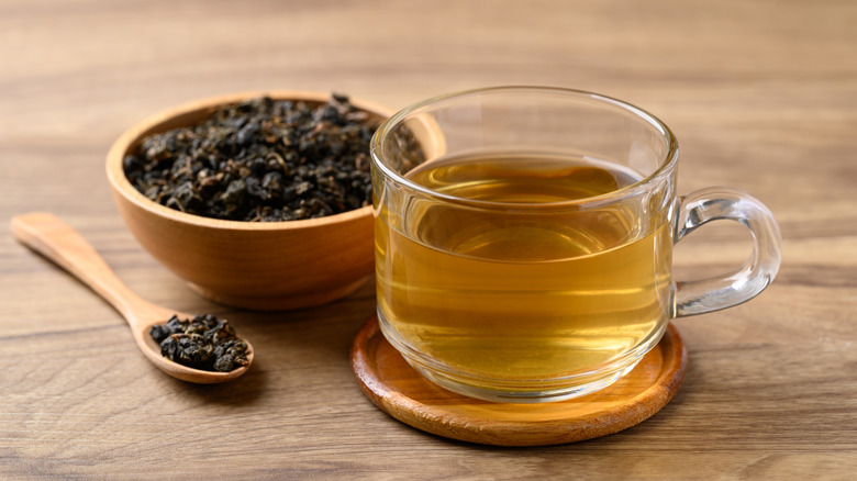 A cup of oolong tea with a wooden bowl of its leaves behind it.