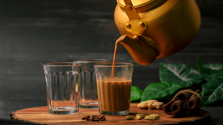 A pot pouring a glass of masala chai, a traditional Indian milk tea.