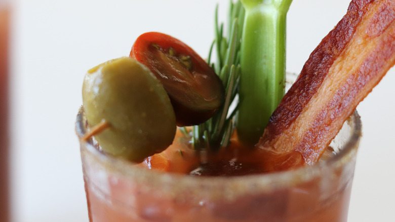 A celery stalk, cherry tomato, and bacon garnishes on a Bloody Bull cocktail