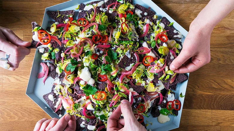 Bobby Flay's nachos with Brussel sprouts on a six sided tray with hands reaching in