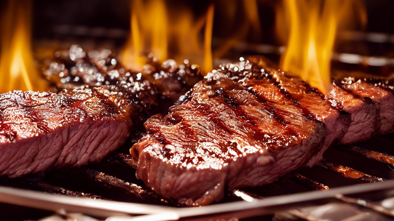 Two steaks with sear marks cooking on a flaming grill