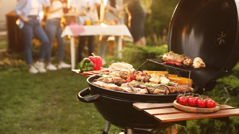 Kebabs, steaks, and corn being cooked on a grill at an outdoor cookout event