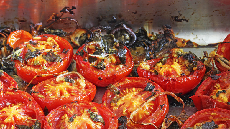 Halved roasted tomatoes with herbs on a metal surface