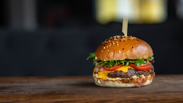 A burger with a toothpick in the middle on a wooden board.