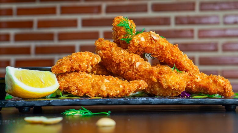 Crispy coated chicken tenders on a board with lemon