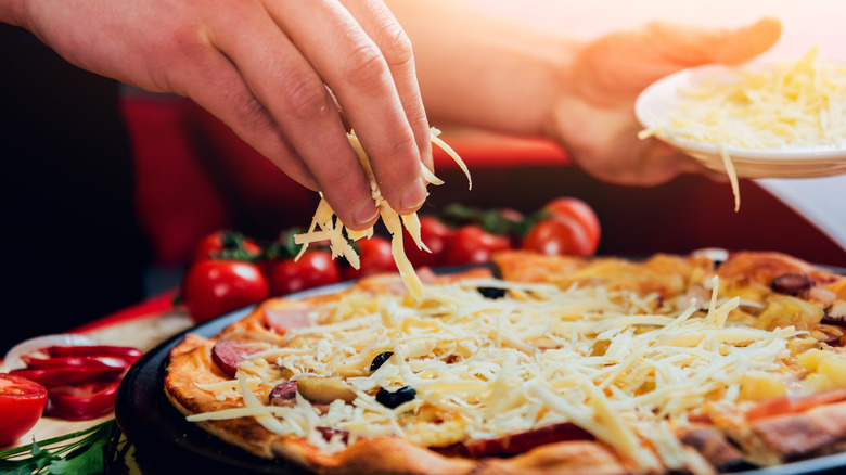 person adding cheese to pizza