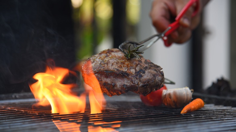 Person puts a steak on a grill as flames come up