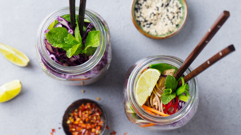 Soba noodles, vegetables, herbs, and lime in glass jars with chopsticks
