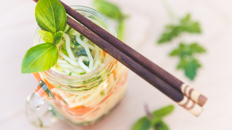 Udon noodle soup with vegetables and basil in glass jar with chopsticks