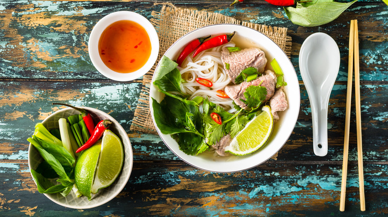 Bowl of beef pho with lime, herbs, and chilies