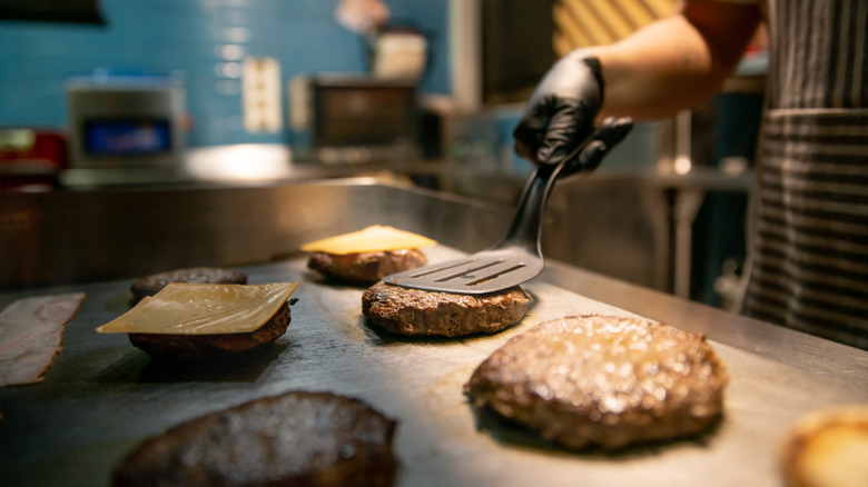 Person cooking burgers on fast food griddle