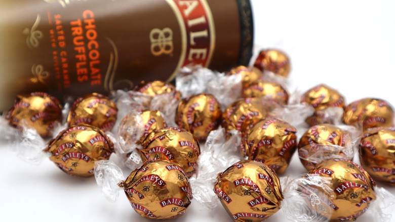 An array of Bailey's chocolates are covered with gold wrappers and sit in front of a Bailey's truffle box