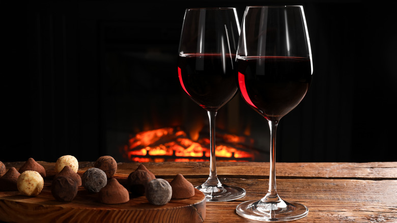 Red wine and chocolate truffles on wooden table with fireplace lit in the background.