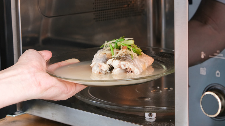 hand taking plated fish out of microwave