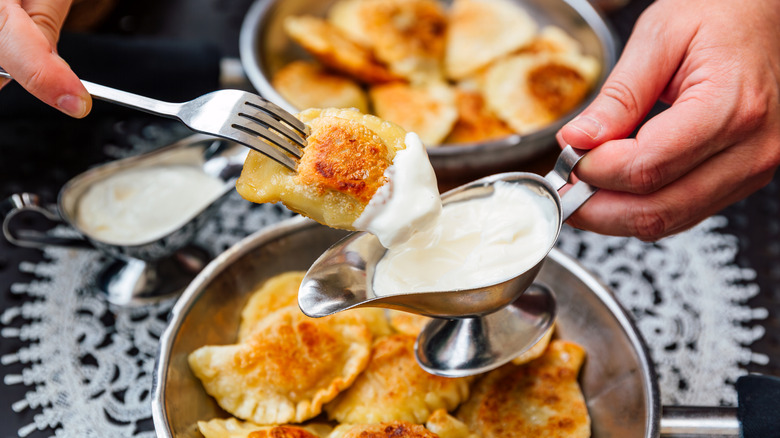 Person dipping pan-fried pierogi into cream sauce