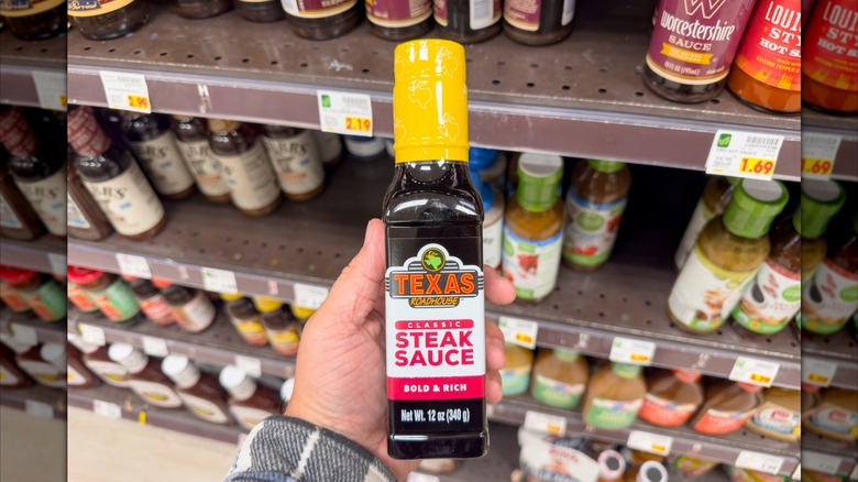 Someone holding a bottle of Texas Roadhouse steak sauce in a grocery store