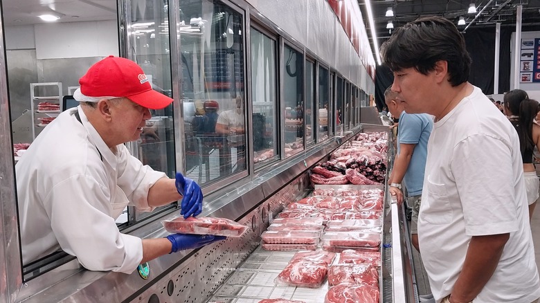 A Costco butcher speaks to a customer through a window