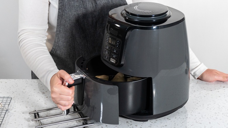 Woman pulling out the basket compartment of a black air fryer