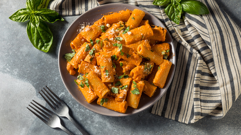 Bowl of pasta alla vodka surrounded by basil leaves and forks