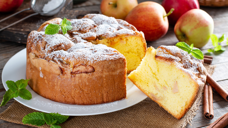 Sponge cake topped with fresh mint on a wooden table with apples and cinnamon sticks