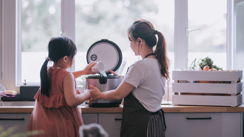 A mother and daughter stand at the counter pouring water into a rice cooker