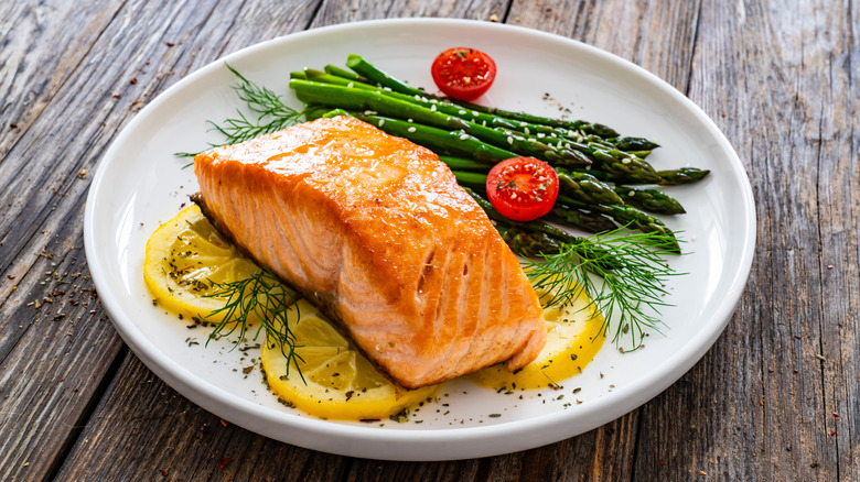 Baked salmon filet on lemon slices, beside it grilled asparagus, all on a white plate