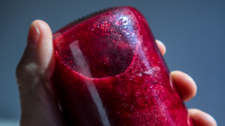 A man's hand holds a glass bottle of magenta juice upside down