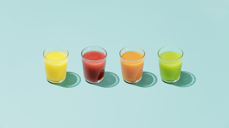 Four glasses of different juice sit against an aquamarine background