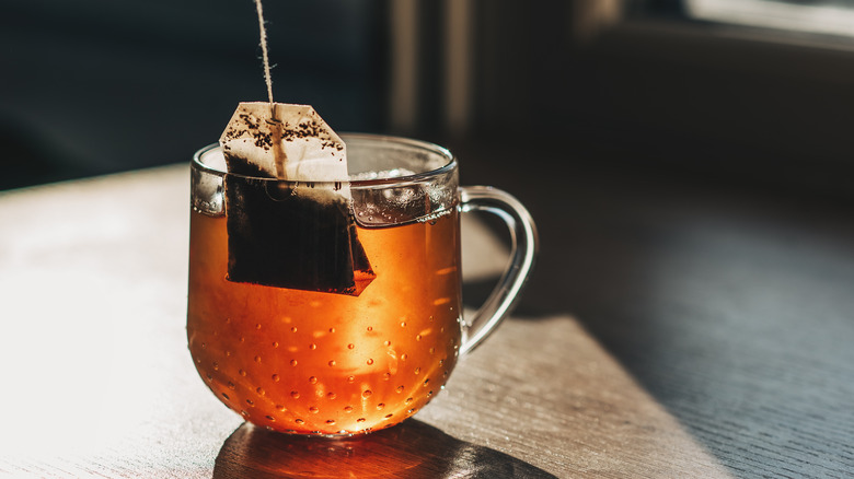 A tea bag inside a glass cup of amber-colored tea