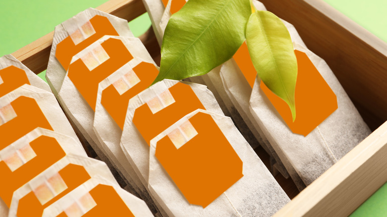 Tea bags sitting in rows inside a wooden box with two fresh tea leaves