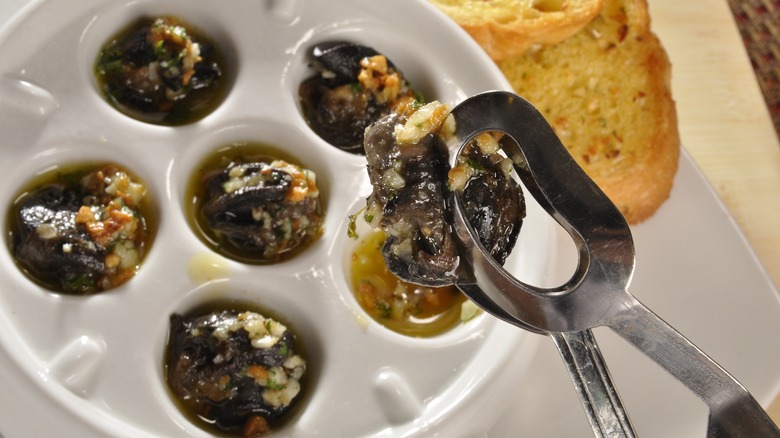 Escargot in garlic butter on white plate with bread and spoon