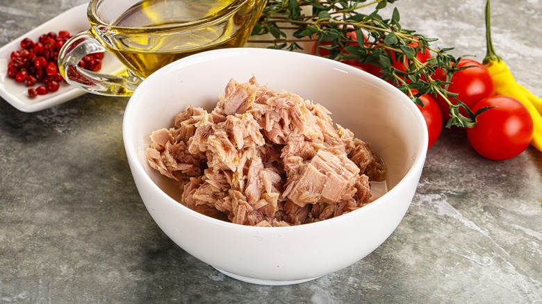 Canned tuna in bowl next to veggies and herbs