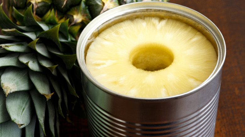 A can of sliced pineapple alongside a raw pineapple top