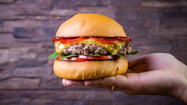 Person's hand holding a burger topped with pepperoni and cheese