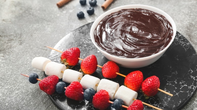Chocolate fondue in a bowl with berries and marshmallows on skewers 