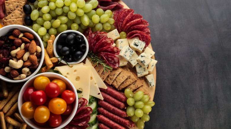 meat, cheese, fruits, vegetables, crackers, and nuts on a plate