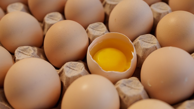 Raw chicken eggs in egg paper box with one egg cracked showing the yolk